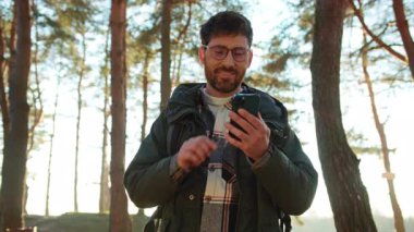 Neşeli Kafkasyalı adam akıllı telefonu elinde tutuyor. Ormanda GPS navigatörü kullanıyor.