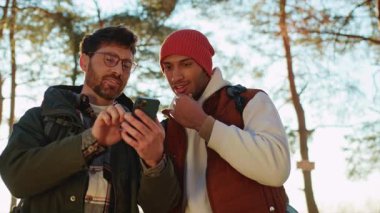 Ormanda akıllı telefon kullanan düşünceli genç, çok ırklı homoseksüel çift.