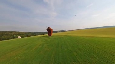 Açık alan. FPV, kulübe kenti yakınlarında hızlı bir uçuş. Hız hareketi. Bordo ve gri heykellerle dolu yeşil alan. Modern sanat. Eklektizm. Havadan takip edin. Geleceğin parkı. Yaratıcı yaratıcılık fikri.