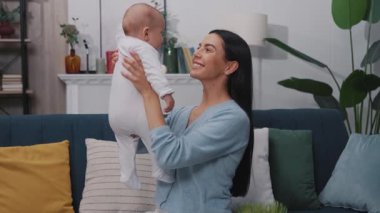 Mutlu genç anne yeni doğmuş bebeğiyle oynuyor ve modern bir dairede bir kanepede oturuyor. Çocukluk. Annelik. Yavaş çekim