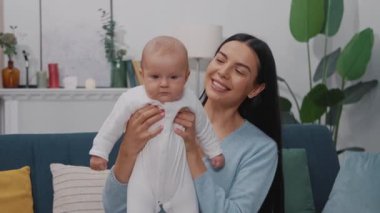 Sevimli bir genç anne yeni doğmuş bebeğiyle oynuyor ve modern bir dairede bir kanepede oturuyor. Çocukluk. Annelik. Yavaş çekim