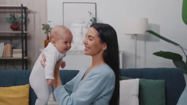 Yakın plan mutlu genç anne, yeni doğmuş bebeğiyle oynuyor. Onu kucaklıyor ve modern bir dairede bir kanepede oturuyor. Çocukluk. Annelik. Yavaş çekim