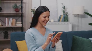 Mavi bir kanepede oturan güzel bir genç kadının portresi ve modern bir odada kameraya bakarak başını çeviren bir akıllı telefon kullanıyor. Tıklıyor, kayıyor. Yavaş çekim