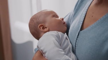 Rahat bir evde annesinin kollarında uyuyan yeni doğmuş bir bebeğin portresi. Annelik. Çocukluk. Anne elini tutuyor, çocuk. Yavaş çekim