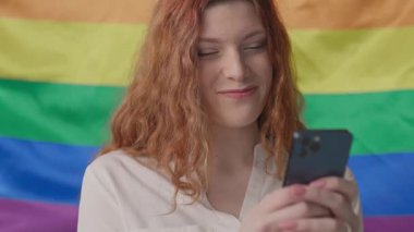 Mutlu kadın arka planda gülümseyen telefon kullanır gökkuşağı renginde bayrak sallar. LGBT