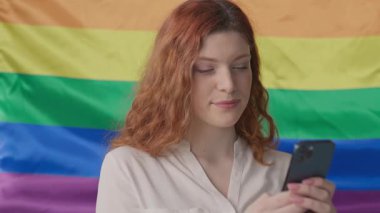 Lezbiyen kadın telefonuyla arka planda gökkuşağı renginde bir bayrak sallıyor.