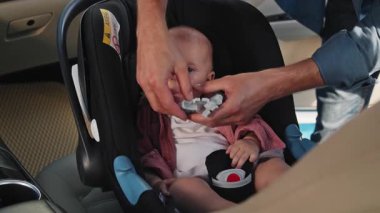 Komik baba, yeni doğmuş bebeğini bebek koltuğuna oturtuyor ve bir çocukla arabaya binerken emniyet kemeri takıyor. Öpüşme. Komik çocuk. Çocukluk. Mutluyum. Yavaş çekim