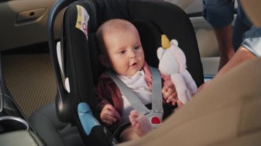 Bebek koltuğunda oturan sevimli küçük kız babası ona oyuncaklar verince mutlu oluyor. Çocuk arabanın içindedir. Araç ve ulaşım konsepti. Seyahat et. Yavaş çekim