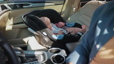 Baba arabada oturuyor, emniyet kemerini küçük kızın yanına bağlıyor bebek koltuğuna oturuyor ve babasının eliyle oynuyor. Çocuk arabanın içindedir. Araç ve ulaşım konsepti. Seyahat et. Yavaş çekim
