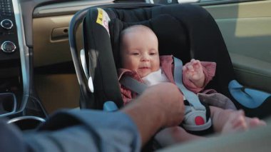 Bebek koltuğunda oturan sevimli küçük kız babasının eliyle oynamaktan mutlu oluyor. Çocuk arabanın içindedir. Araç ve ulaşım konsepti. Seyahat et. Yavaş çekim