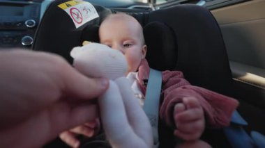 Bebek koltuğunda oturan sevimli bir kız, annesi oyuncaklarını verdiğinde mutlu olur. Çocuk arabanın içindedir. Araç ve ulaşım konsepti. Seyahat et. Yavaş çekim