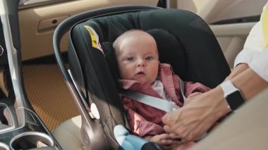 Arabadaki çocuk koltuğunda oturan sevimli, komik, beyaz çocuk. Kadın eli emniyet kemerini çözüyor. Anne oğluyla ilgileniyor. Yardım et, aşkım. Güvenlik koltuğu. Kadın ve bebek. Gündüz vakti. Ulaşım