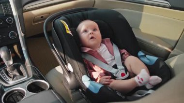 Arabada çocuk koltuğunda oturan güzel, duygusal bir erkek bebek görüntüsü. Anne emniyet kemerini çözüyor, çocuğun burnuna dokunuyor. Ata binerken güvende. Dikkat et, aşkım. Gündüz, yaz, yolcu