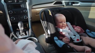 Annesinin yanındaki çocuk koltuğunda oturan komik küçük çocuğun yakın çekim görüntüleri. Otomobilde sürücü koltuğunda oturan kadın. Çocuk gülüyor. Çocukluk, sigorta, yolcu, anne, bakım. Taşıma, kuşak