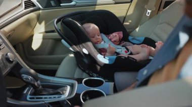 Babam sürücü koltuğunda oturuyor. Çocuk koltuğundaki gülümseyen bebek babaya bakıyor. Beyaz bir adamın oğlunun parmaklarına dokunduğu görüntüler. Otomobil içi