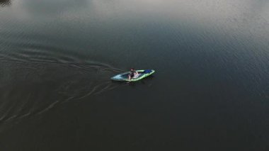 Huzurlu göl manzarasında küçük bir kayıkta uçan genç adamın görüntüsü. Dağlardaki sinematik nehir. Orman ve tepeler. Doğal ortam. Spor, eğlence..