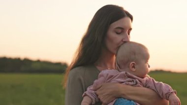 Anne nazikçe kızının başını öpüyor. Birlikte güzel günbatımına hayran kalıyorlar. Çocuk ve mutluluk kavramı.