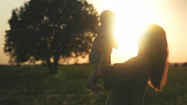 Gülümseyen, heyecanlı beyaz bir kadının, arka planda yaşlı bir ağacın arkasında küçük sevimli bir çocuğu tutarken çekilmiş görüntüler. Ağır çekim. Arka plan bulanık. Şehir dışında. Yaz akşamı.