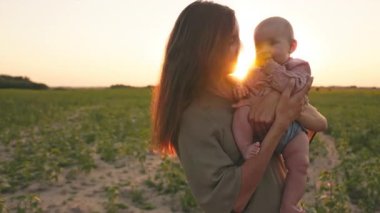 Sevimli anne, tatlı çocuğu sakinleştiriyor, sahada bebeği öpüyor. Gülümseyen beyaz bir kadının portresi güzel bir günbatımının arka planında elinde bebekle duruyordu. Yaz zamanı, akşam dışarıda