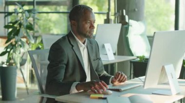 Bilgisayarda oturup klavyede daktilo çalan kendine güvenen bir Afrikalı 'yı çekmek. Gri takım elbiseli ve kameraya bakan kendine güvenen iş adamının portresi. Kapalı