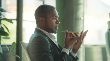 Yakışıklı, kendinden emin, orta yaşlı, akıllı telefonlu ve işçilere sesli mesaj kaydeden bir iş sahibi. Gri takım elbiseli çekici iş adamının portresi. İçeride. Yatay görünüm