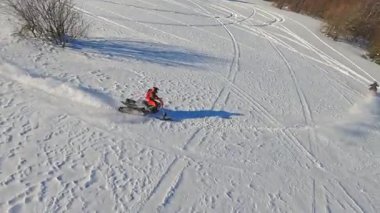 Dağlardaki insansız hava aracı görüntüsü, kar motosikletli iki adam kışın güneş ışığında atlar ve ata binerler.