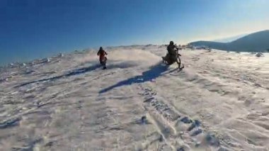 Dağlardaki güzel hava manzarası, kar motosikletli iki adam kışın güneş ışığında atlayıp geziyorlar.