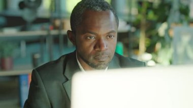 Bilgisayarda çalışan yakışıklı Afro-Amerikan adam masasındaki ofiste ciddi ciddi ekranlara bakıyor. Güneş ışığı. Şirket. Başkanım. İş adamı. Yavaş çekim