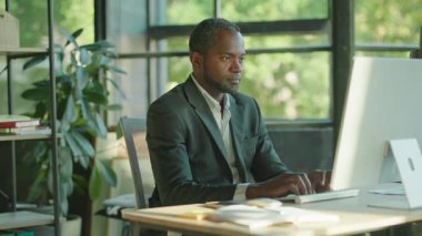 Yorgun Afrikalı Amerikalı iş adamı bilgisayar ekranına bakıyor ve acı çekiyor. Stres yüzünden. Çok çalıştım. İş adamı. Yavaş çekim