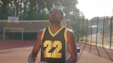 Çekici Afrikalı Amerikalı atletlerin top attığı görüntüler. Açık hava eğitimi sırasında kameraya bakan güler yüzlü bir adam. Basketbol potası. Spor konsepti. Başla. Şehir hayatı, şehir hayatı. El pozisyonu. Yaz zamanı, güç.
