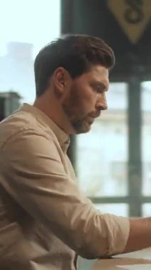 Bu video beyaz gömlekli, işine odaklanmış bir adamı gösteriyor. Ayarlar arasında hareket eder, dizüstü bilgisayar kullanırken çenesini sıklıkla dinlendirir.