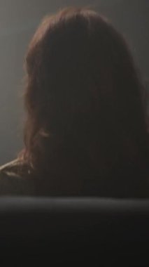 Yeşil kazaklı bir kadın loş bir odada cep telefonu ve tabletle etkileşime girer. Vitray pencerenin yanında. Teknolojinin etkisini yansıtır.