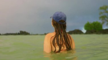 Bu sakin videoda, mavi şapkalı bir kadın sakin sularda duruyor, huzuru yansıtıyor. Beyzbol şapkalı başka bir kadın daha katıldı, neşe ve keşfin somutlaştırıcısı.