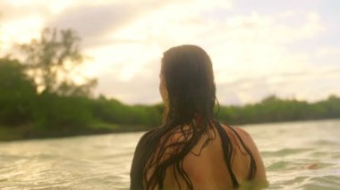 Sakin bir video günbatımında sakin sularda bir kadını gösteriyor. Bir gölde duruyor, görüntüye dalmış, sonra okyanusta zarafetle yüzüyor, doğayla bağ kuruyor.