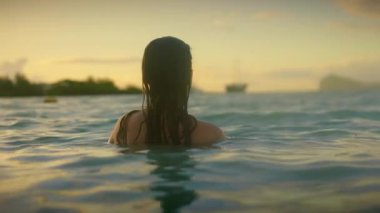Sakinleştirici bir video günbatımında okyanusta yüzen bir kadını ve sakin bir havuzu gösteriyor. Güzelliği ve rahatlığı ön plana çıkarıyor.