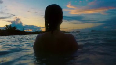 Gün batımında okyanusta zarif bir şekilde yüzen bir kadın gibi sakin bir sahne ortaya çıkıyor. Gökyüzünün renkleri suyu yansıtıyor ve güzel bir zemin oluşturuyor.