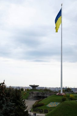 Rüzgarda dalgalanan Ukrayna bayrağı, Anavatanın ünlü heykelinin yanında. Mavi gökyüzündeki Ukrayna 'nın en büyük ulusal bayrağı. Güzel sonbahar manzarası. Ukrayna, Kyiv - 9 Ekim 2022
