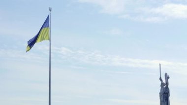 Ukrayna bayrağı rüzgarda dalgalanıyor mavi gökyüzüne karşı, Anavatan 'ın ünlü heykelinin yanında. Ünlü manzaralar, anıtlar ve Kyiv anıtları. Ukrayna, Kyiv - 08 Ekim 2022