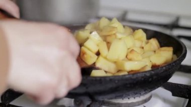 Bir kadının eli kızarmış patatesleri tavada ahşap bir spatulayla karıştırır. Ayçiçeği yağıyla dökme demir bir tavada taze patates pişirme işlemi. Kızarmış patatesle dolu bir tava.