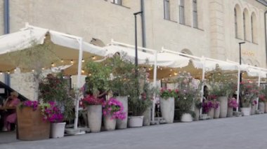 Tepe örtüsünün altında rahat bir sokak kafesi, yaya bölgesinde masalar. İnsanlar açık hava restoranlarında yemek yiyip konuşuyorlar. Lokantadaki yerli ve turistler. Ukrayna, Kyiv - 9 Haziran 2022