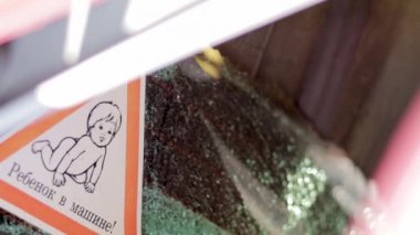 Warning sign of children inside a car after an accident with broken glass. Translation: Child in the car. A close-up of a child on a sticker, on the rear window of a car