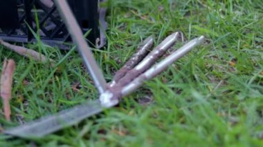 Bahçe aleti, plastik kutuların arka planında bahçıvanlık yapmak için helikopter tırmıklıyor. Bahçe işleri ve sürdürülebilir yaz konsepti. Doğal bir arka planda tırmık ve çapa ile metal bahçe aracı