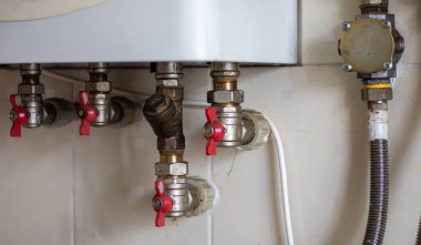 Fayanslı bir duvara gaz kazanını bağlamak için gizli su muslukları. Yerel bir çift devirli gaz kazanının tesisat bağlantıları. Isıtma sisteminin boruları. Kırmızı musluklu bir gaz kazanı kuruluyor.