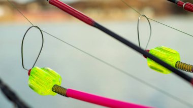 Isırık alarmı suyun arka planında bir oltaya asılı. Gölde, nehirde balık tutarken olta. Balık oltası. Sazan oltası tezgahta, ısırık alarmı açık.