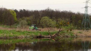 Traktör ormanın içinde bir nehrin ya da gölün kıyısında yol alır..