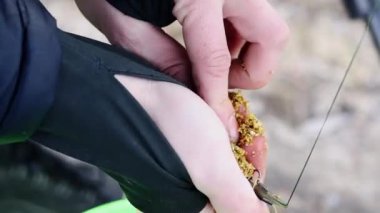 Balıkçı balık yemliğini besleyiciye koyar. Balıklar için yemi hazırlayan tanınmayan bir balıkçının ellerini yakın plan çekiyoruz. Yaşam tarzı kavramı, doğadaki eğlence. Adam balık yemi pişiriyor..