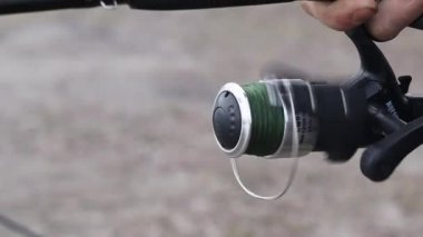 Erkek ellerinin oltada makarayı döndürdüğü yakın plan. Ağır çekim. Yeşil olta ipi yaralı. Doğada eğlence ve hobi kavramı. Ukrayna, Kyiv - 5 Mart 2023.