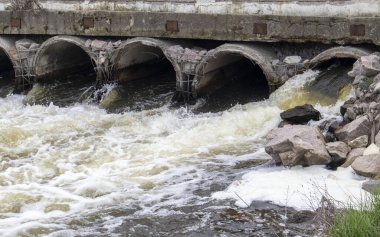 Borulardan nehire pis kokulu, kirli atık su taşıyan beton bir boru. Çevre ve su kaynaklarının kirliliği. Ekolojik felaket. Tehlikeli atık su