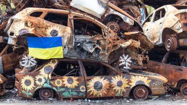 Ukrayna 'nın ulusal bayrağı harabelerin ve harap olmuş arabaların paslı metallerinin arka planına karşı. Harabe bir şehirde güneşin altında dalgalanan mavi-sarı bir bayrak. Ukrayna, Kyiv - 29 Nisan 2023