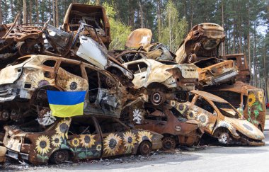 Ukrayna 'nın ulusal bayrağı harabelerin ve harap olmuş arabaların paslı metallerinin arka planına karşı. Harabe bir şehirde güneşin altında dalgalanan mavi-sarı bir bayrak. Ukrayna, Kyiv - 29 Nisan 2023